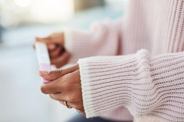 A woman's hands holding a pregnancy test. She is wearing a pink jumper and the background is blurred