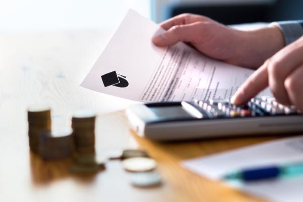 Man counting college savings fund, tuition fee or student loan with calculator. Education price and expenses concept. Mo<em></em>ney and papers on table. Calculating budget and planning finance.