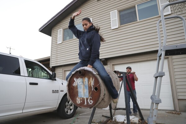 Najiah Knight uses a practice barrel to work on bull riding skills with the help of her father, Andrew, at the family's home in Arlington, Ore., Wednesday, Oct. 18, 2023. Najiah, a high school junior from small-town Oregon, is on a yearslong quest to become the first woman to compete at the top level of the Professio<em></em>nal Bull Riders tour. (AP Photo/Amanda Loman)