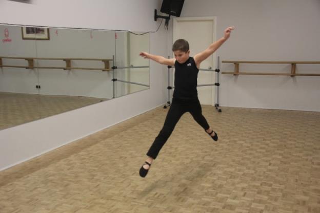 A boy leaps ballet-style in a dance room.